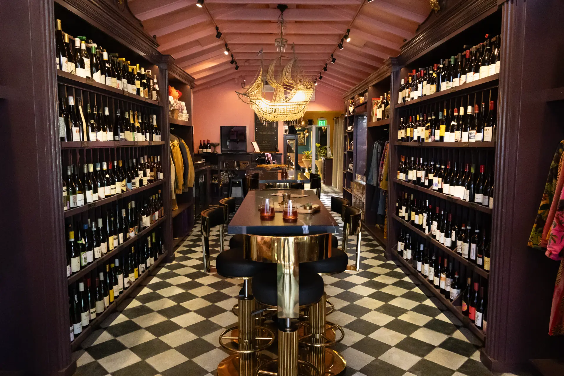 A warm bottle shop interior lined with tall shelves of wine, brass stools and a checkerboard floor