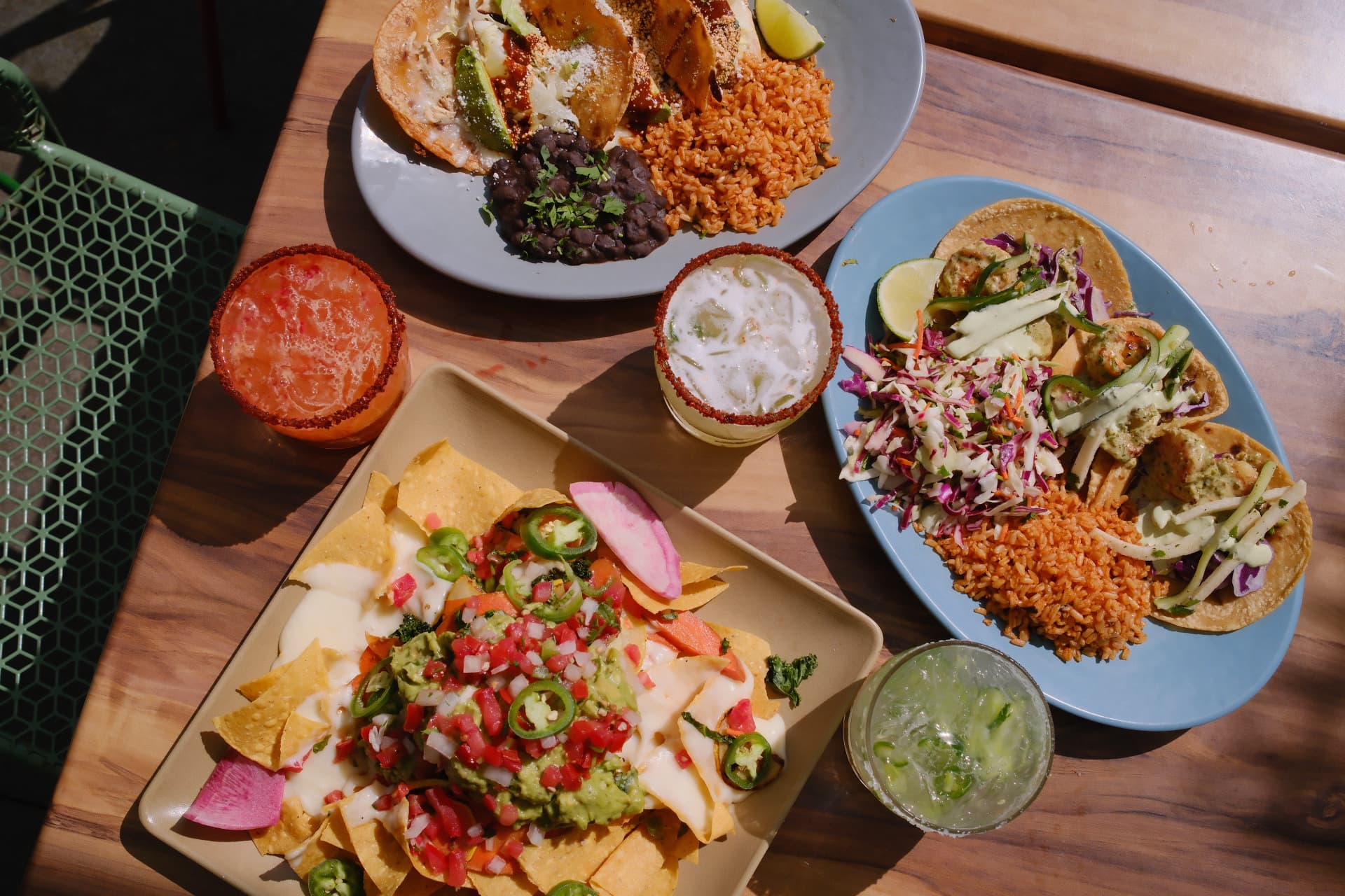 Tacos, nachos and margaritas on a sunlit wooden table at Blue Plate Taco